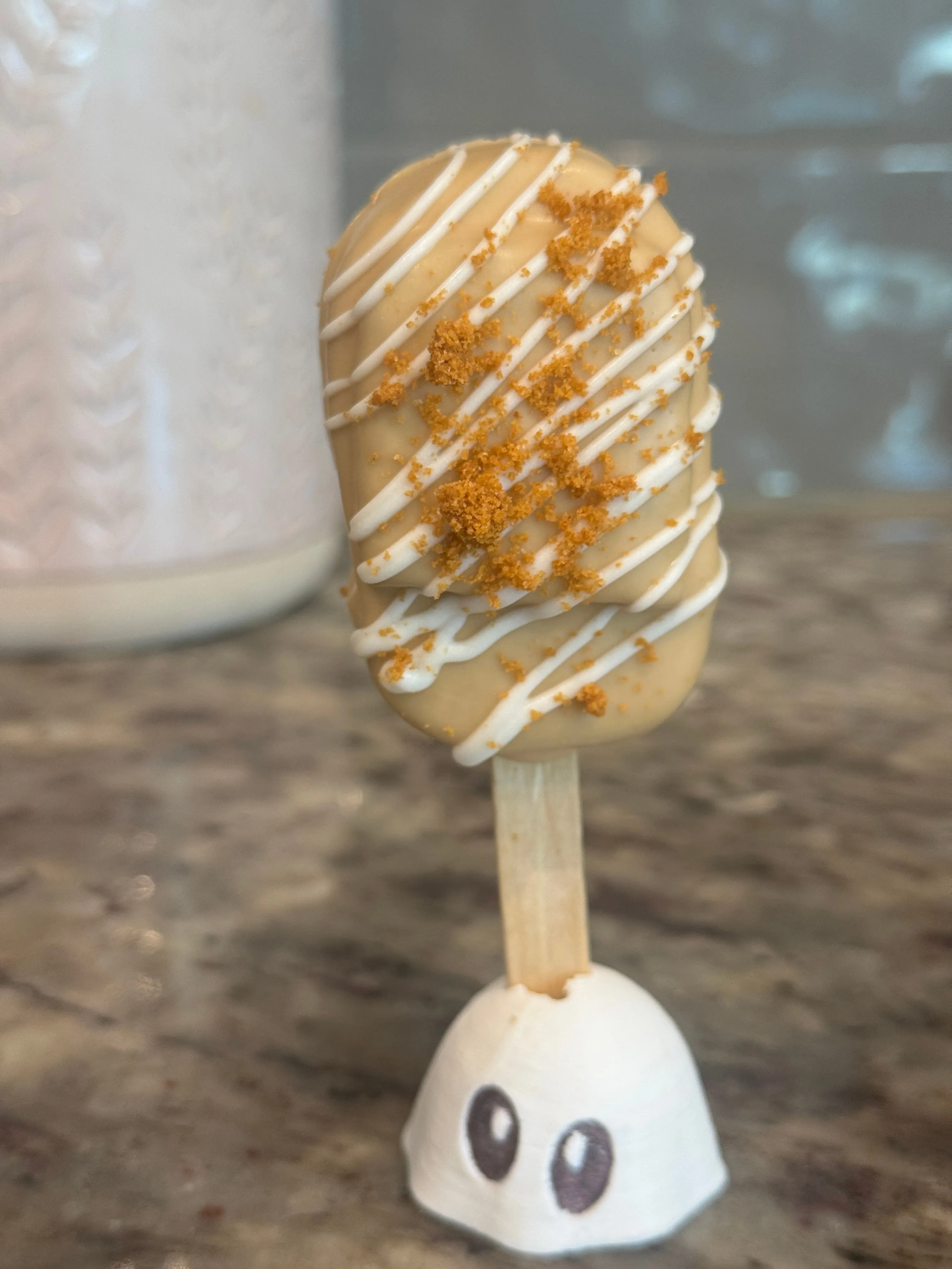 Cookie butter Biscoff cakesicle in a caramel shell with white drizzle and cookie crumbs