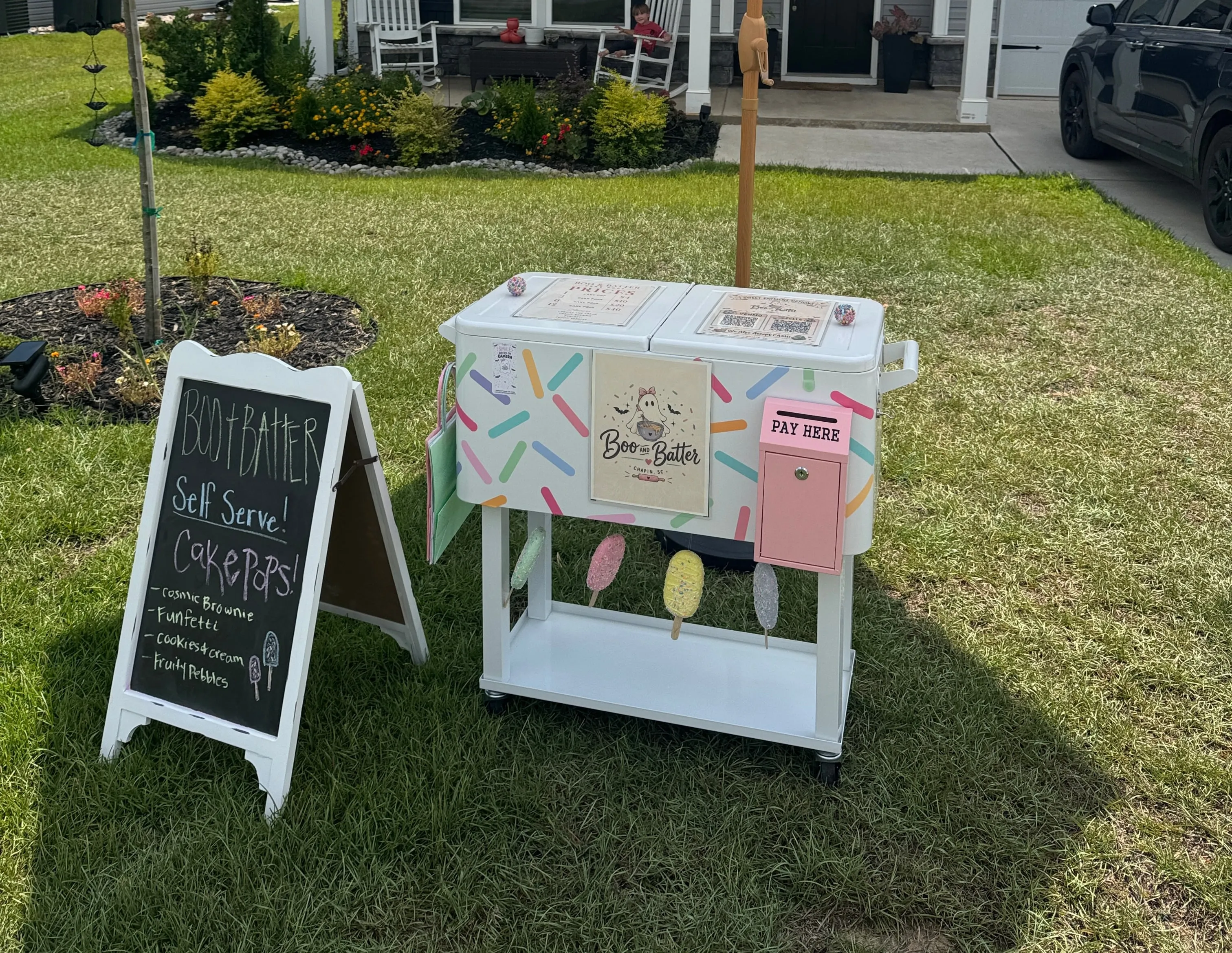 The Boo & Batter self-serve cake pop cart set up on the lawn with a chalkboard menu