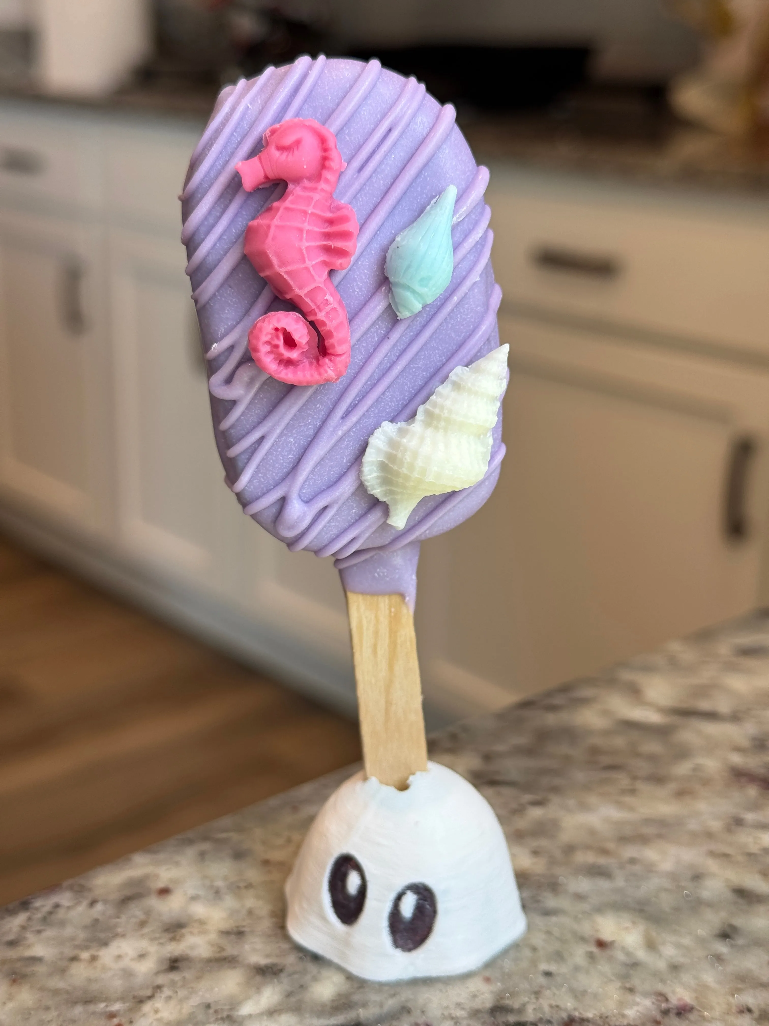 Lavender chocolate funfetti cakesicle with a coral seahorse and cream and aqua shells