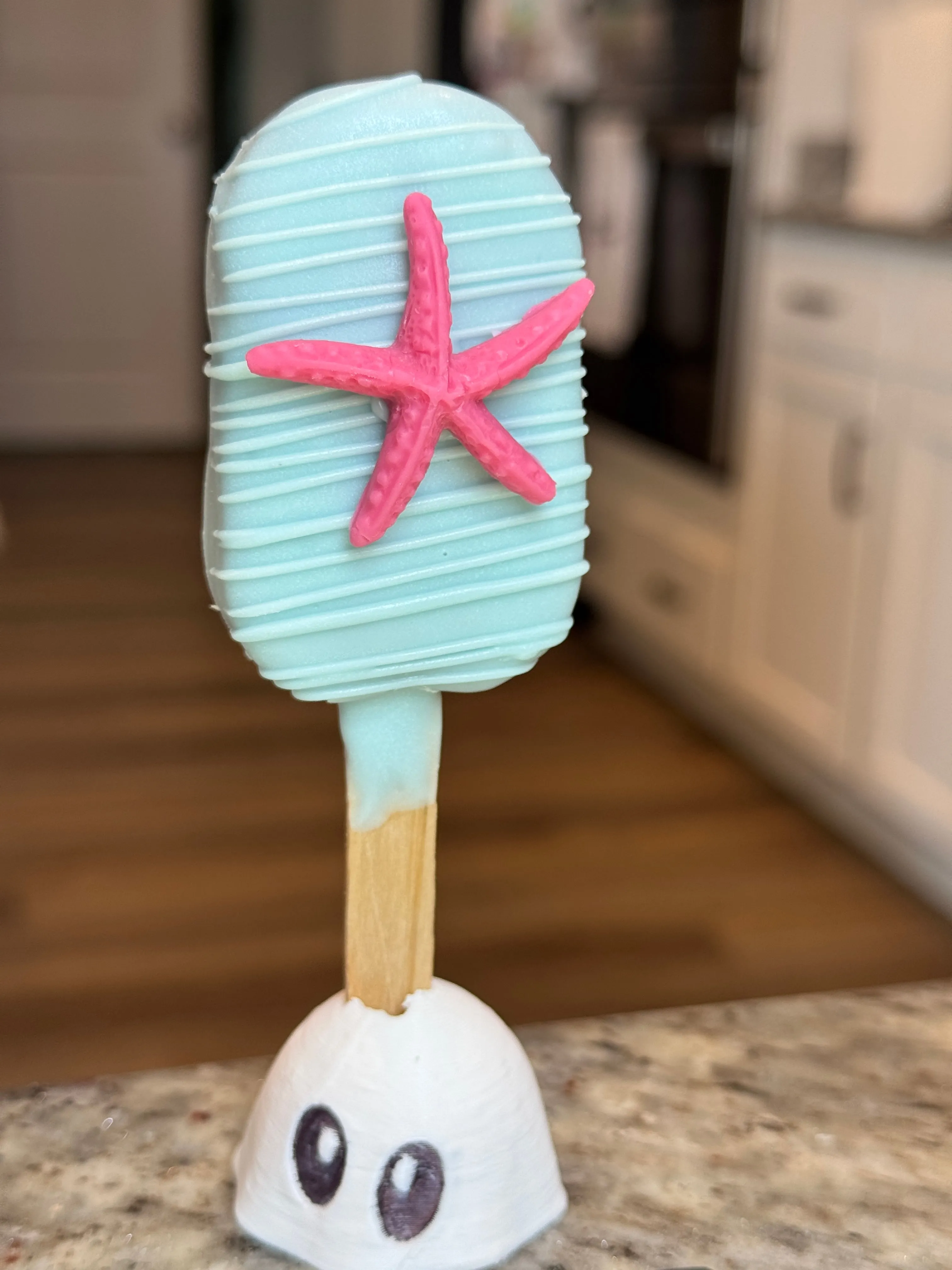 Pale aqua chocolate funfetti cakesicle with white drizzle and a pink chocolate starfish