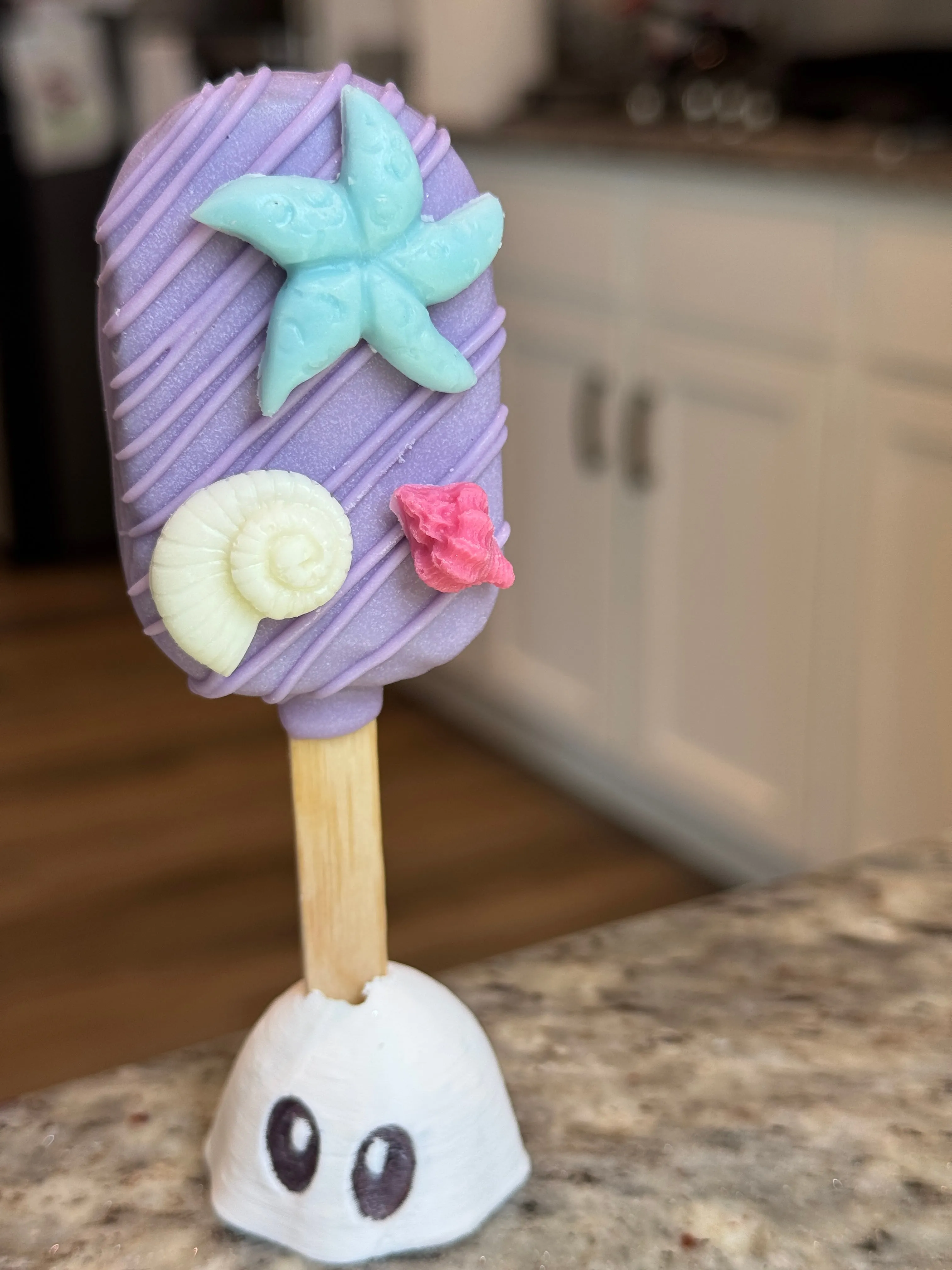 Lavender chocolate funfetti cakesicle with an aqua starfish, cream nautilus shell and coral shell