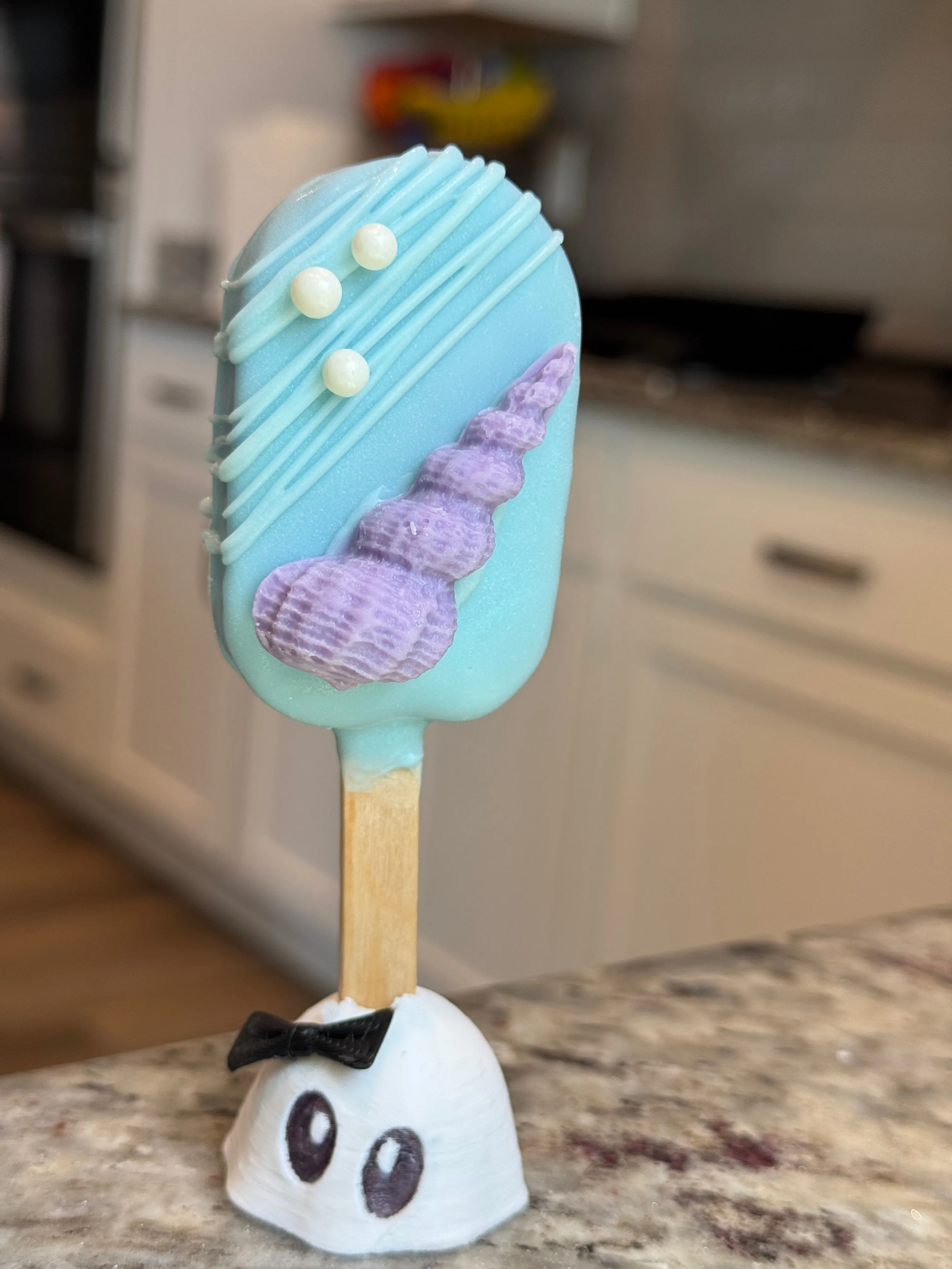 Aqua chocolate funfetti cakesicle with a purple spiral shell and pearl accents