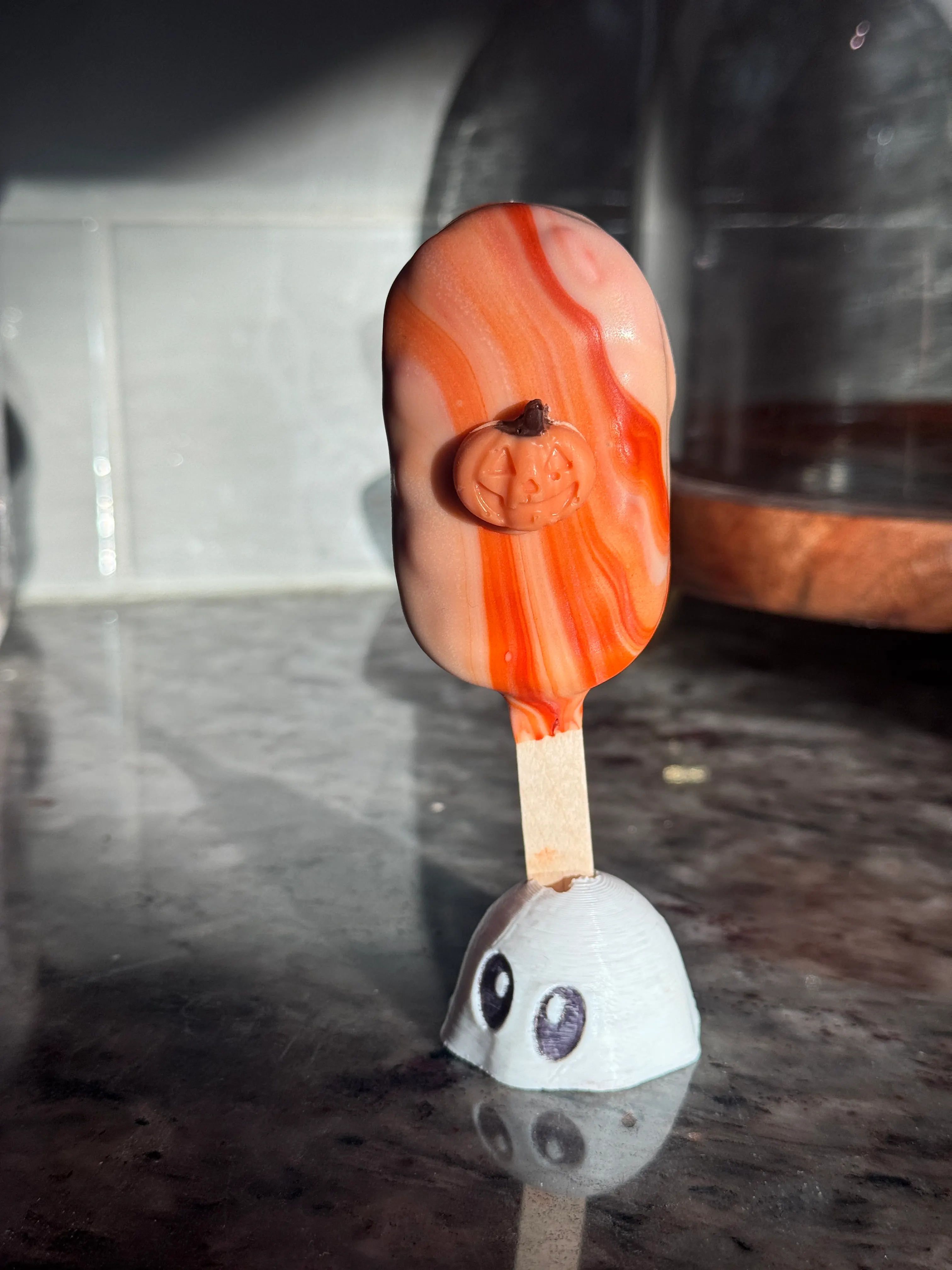 Pumpkin roll cakesicle in an orange and cream marbled shell topped with a little fondant pumpkin