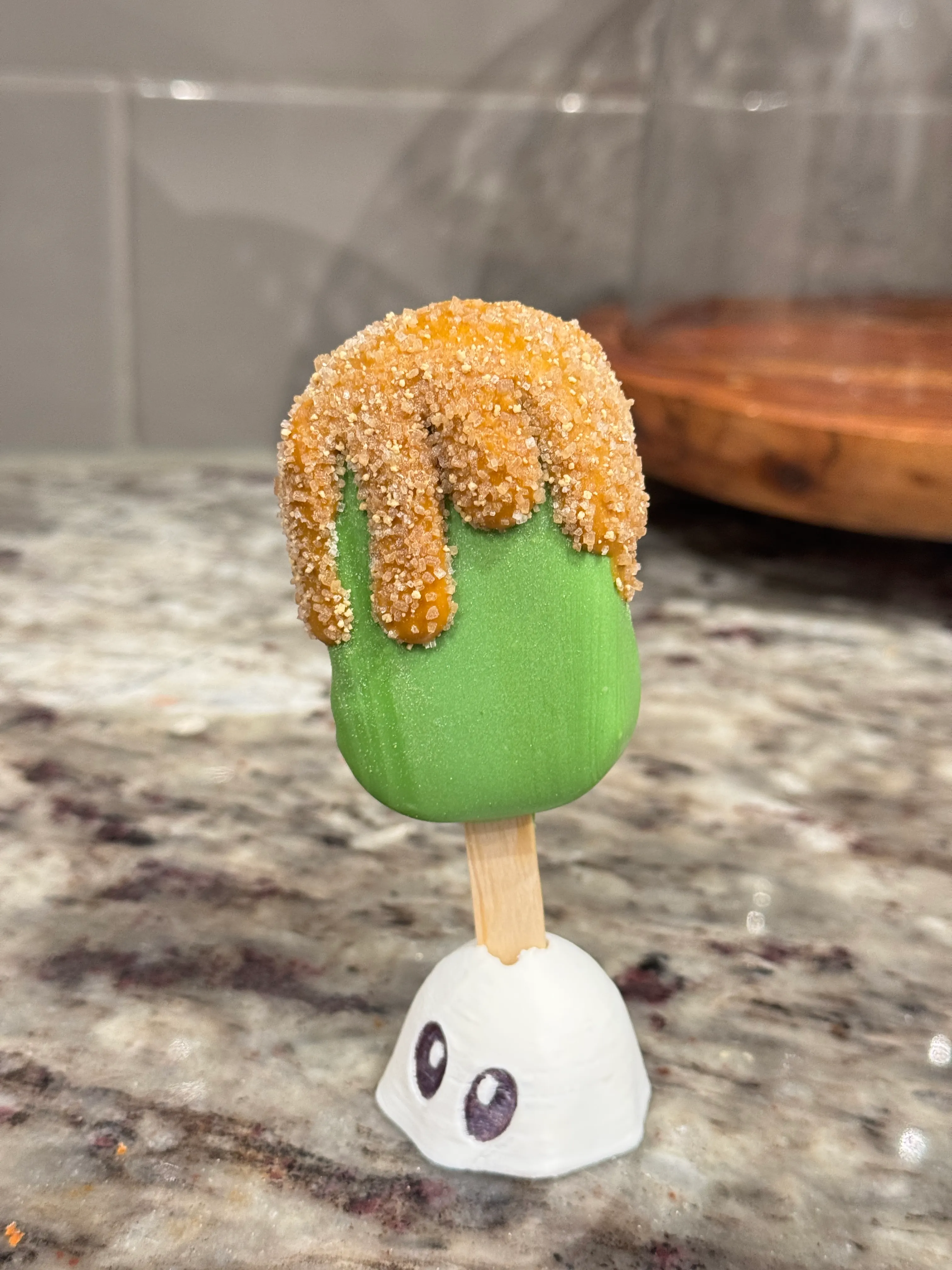 Salted caramel apple cakesicle in a green shell with caramel drizzle covered in coarse sugar crystals