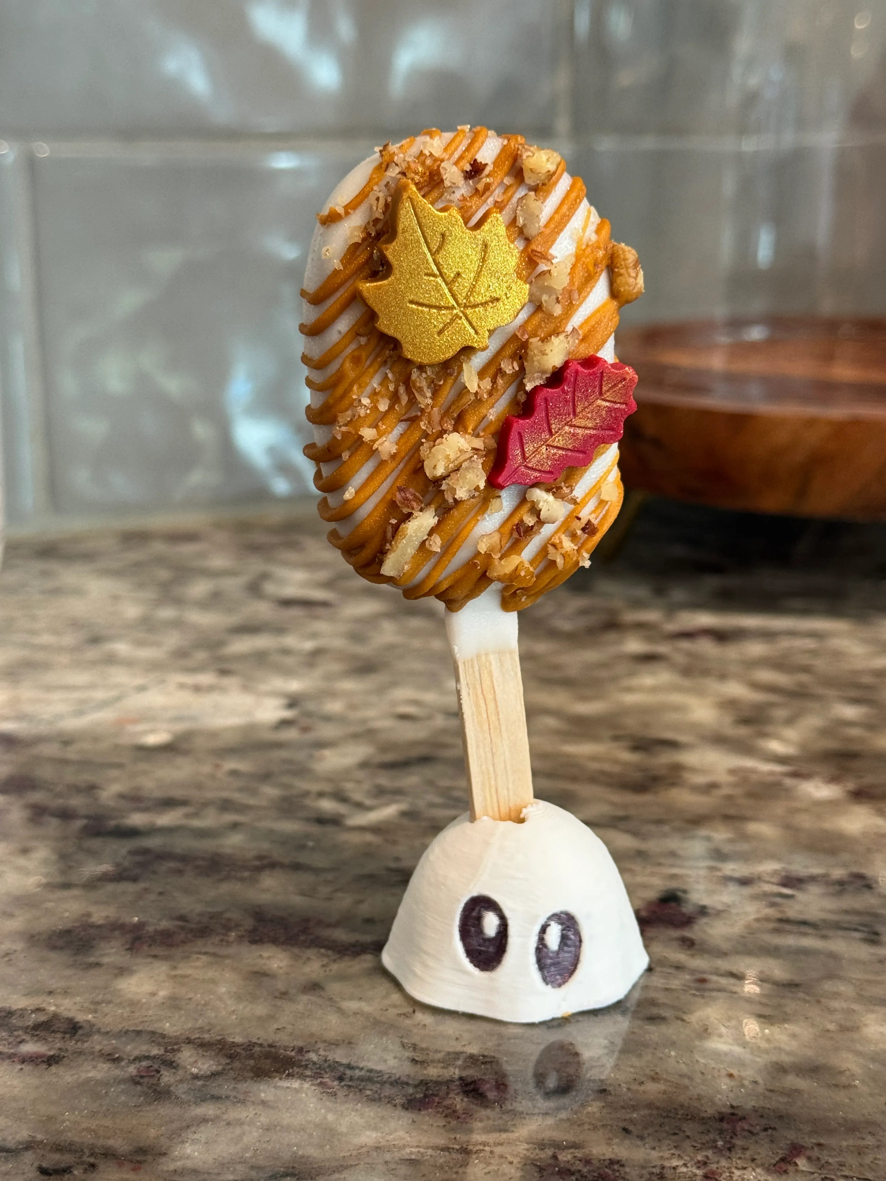 Salted maple pecan cakesicle with caramel drizzle, chopped pecans and gold and red fondant leaves