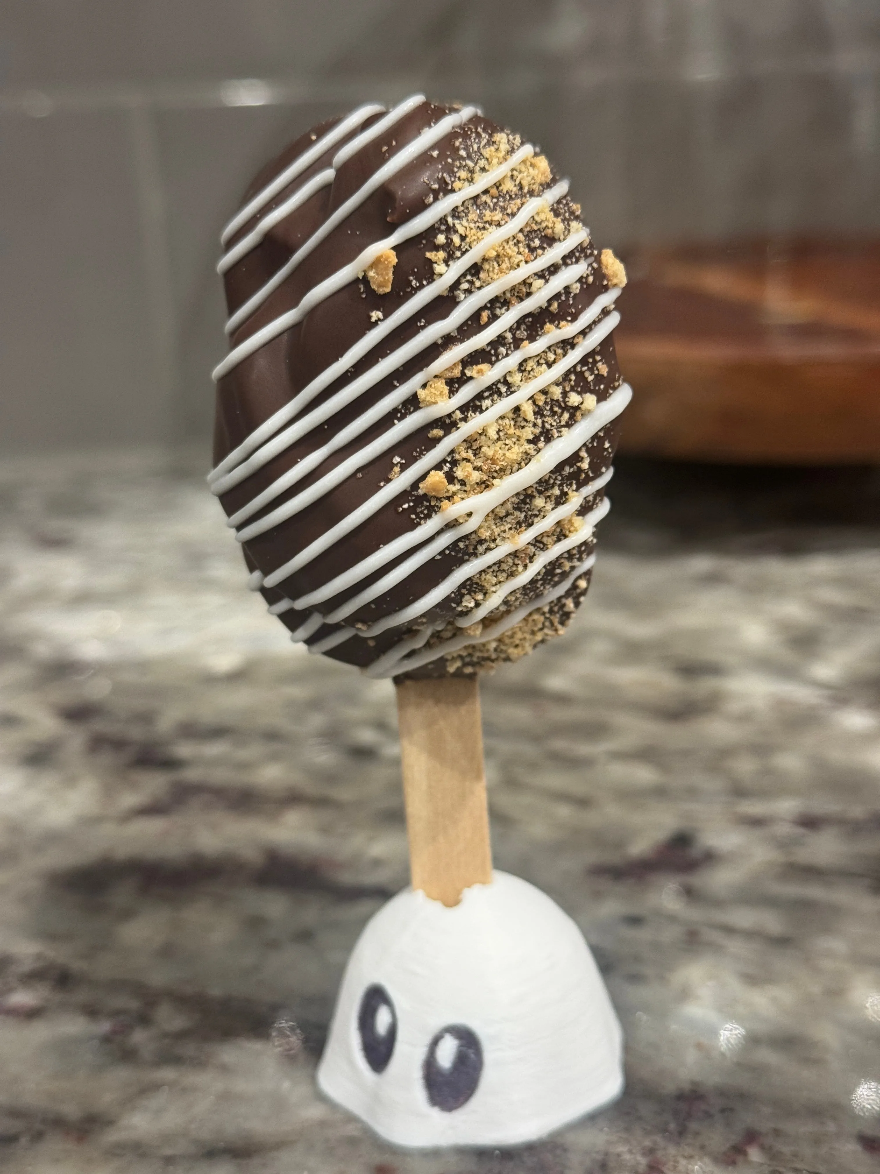 S’mores cakesicle in dark chocolate with white drizzle and graham cracker crumbs