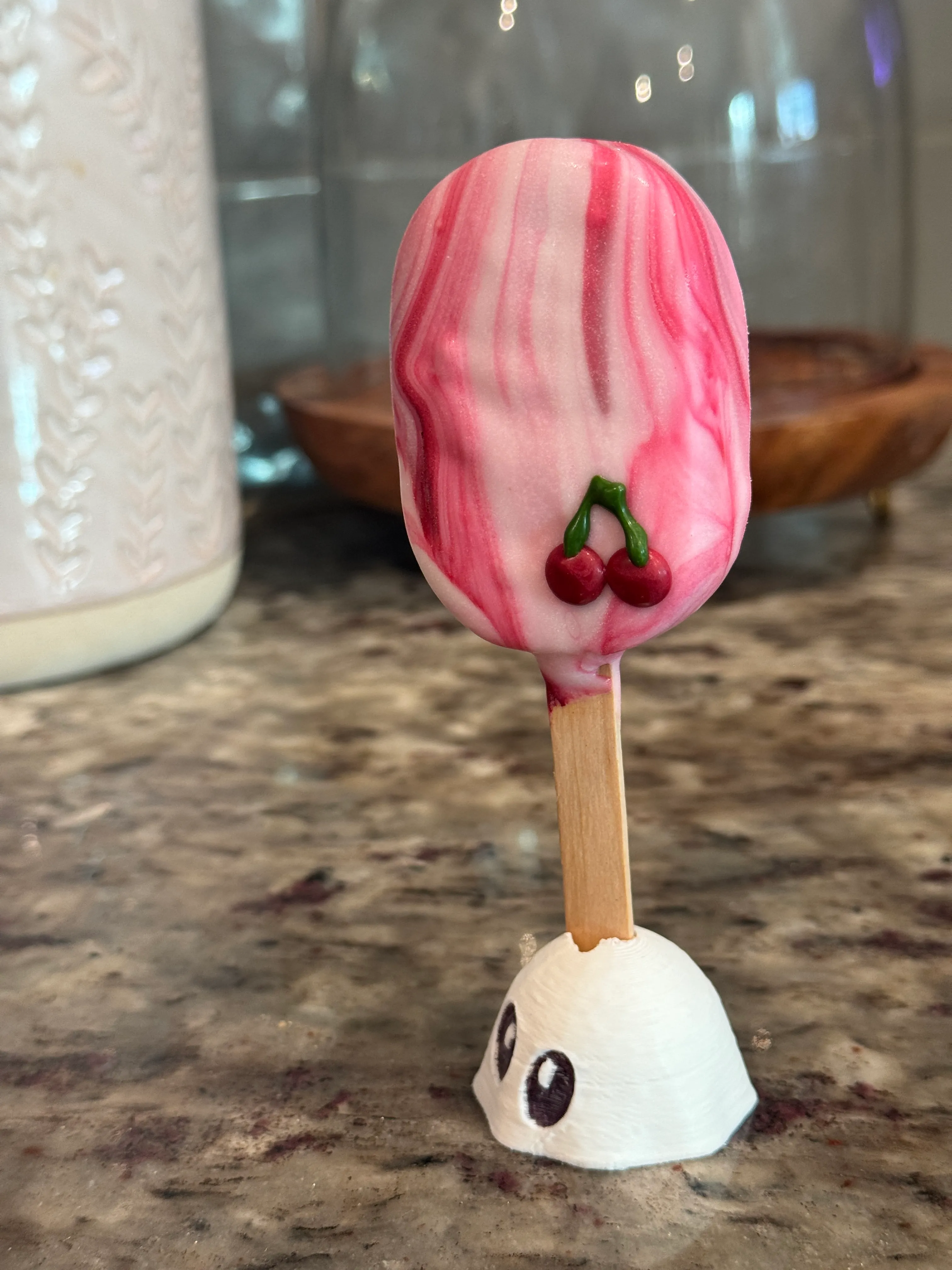 Cherry pie cakesicle in a pink and white marbled shell with two piped cherries