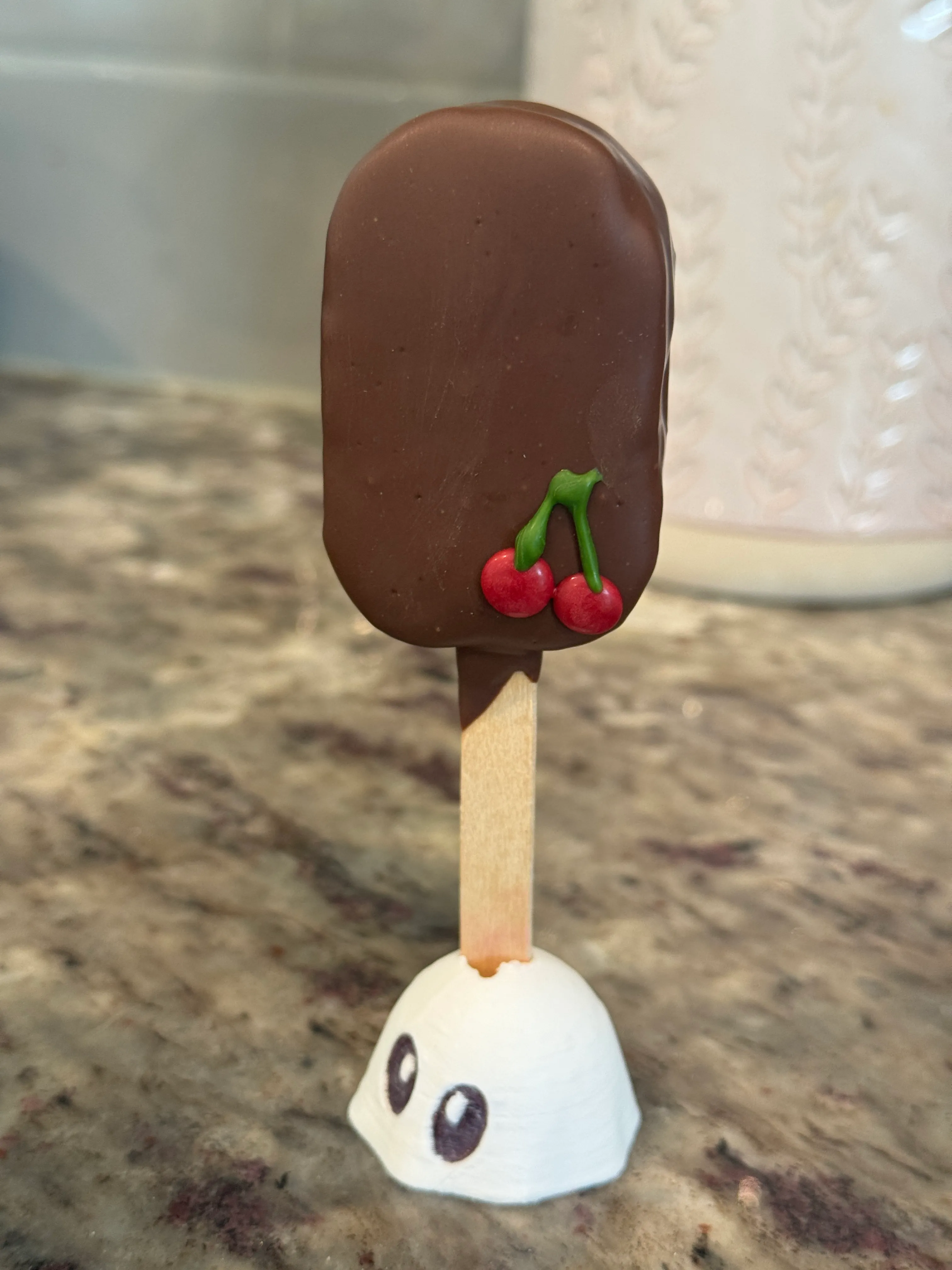 Chocolate cherry cakesicle in a milk chocolate shell topped with two piped red cherries