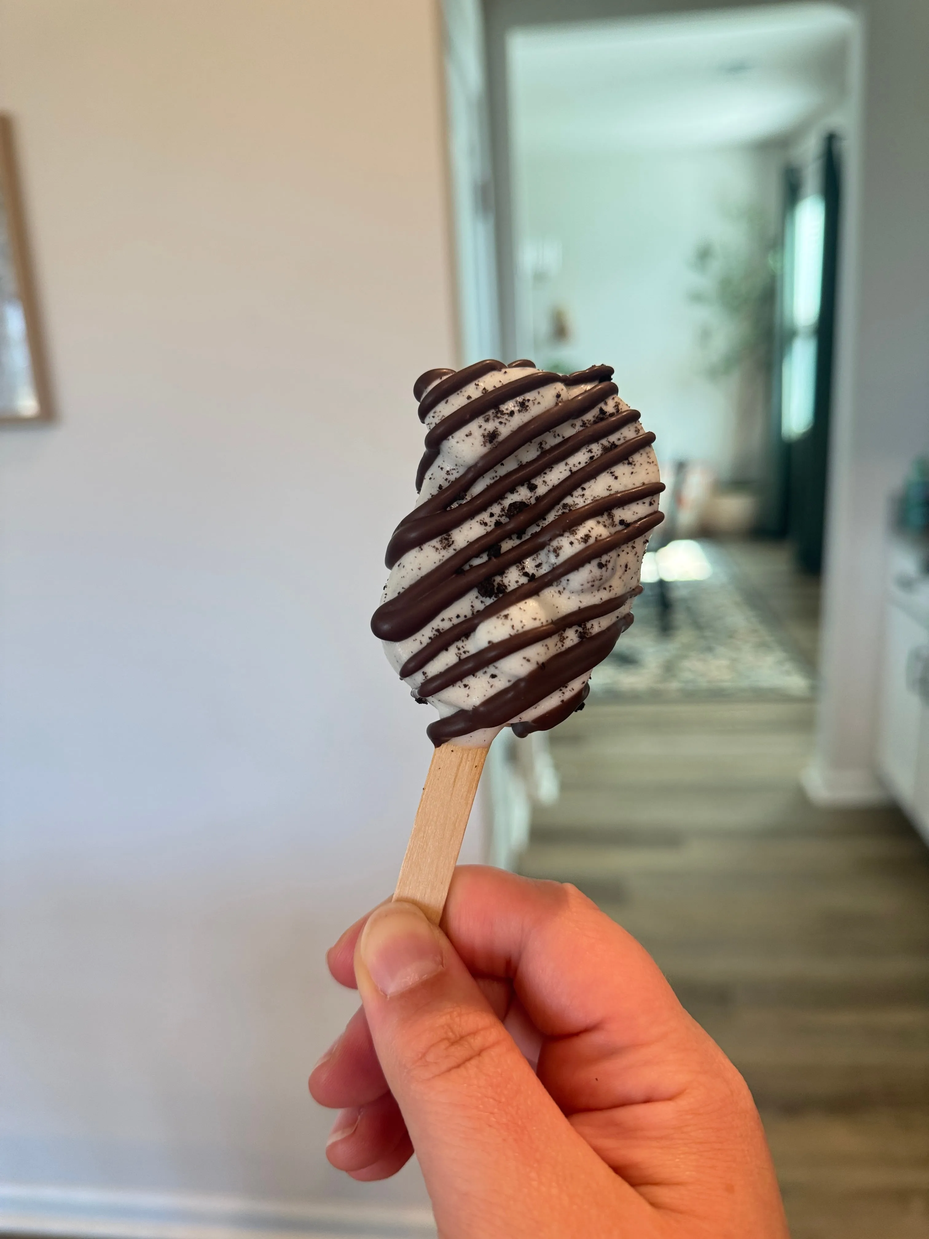 Cookies and cream cakesicle in a white shell with cookie crumbs and dark chocolate drizzle
