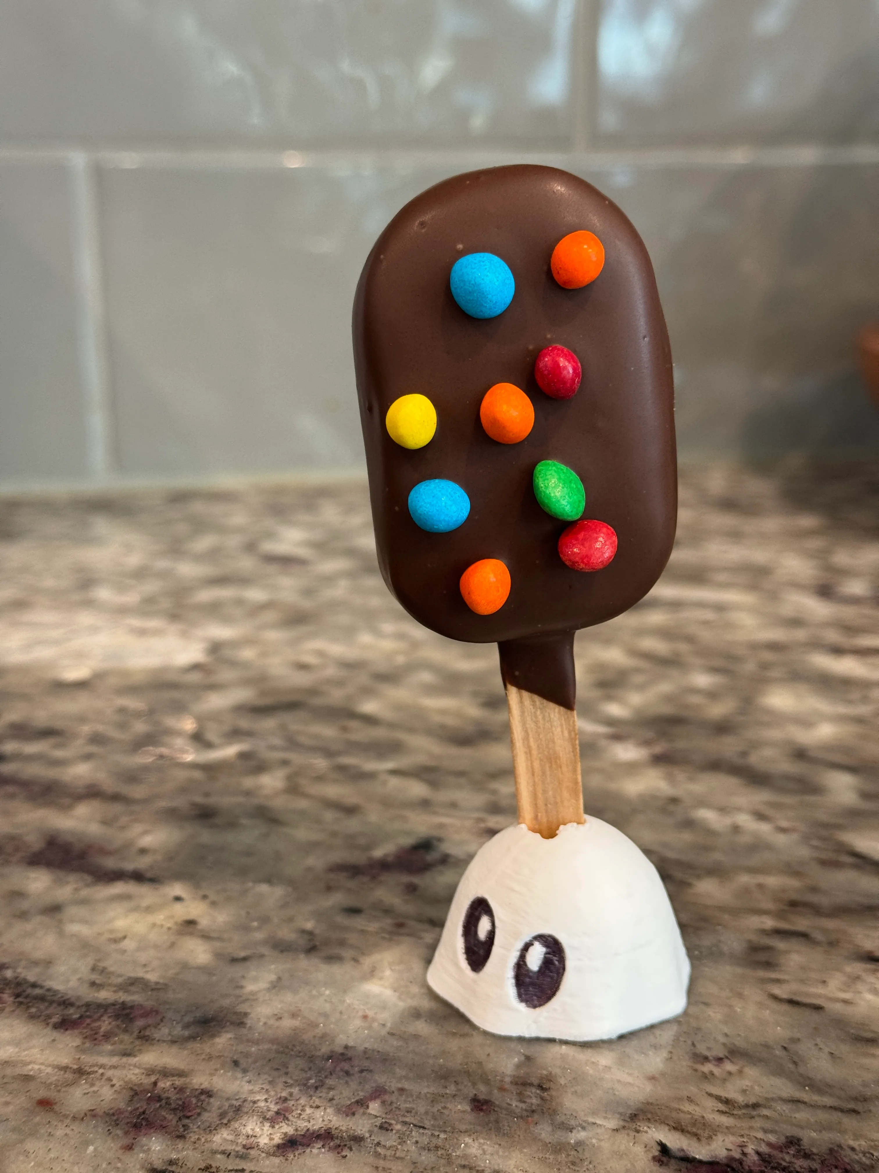 Cosmic brownie cakesicle in a dark chocolate shell topped with rainbow candy-shell pieces