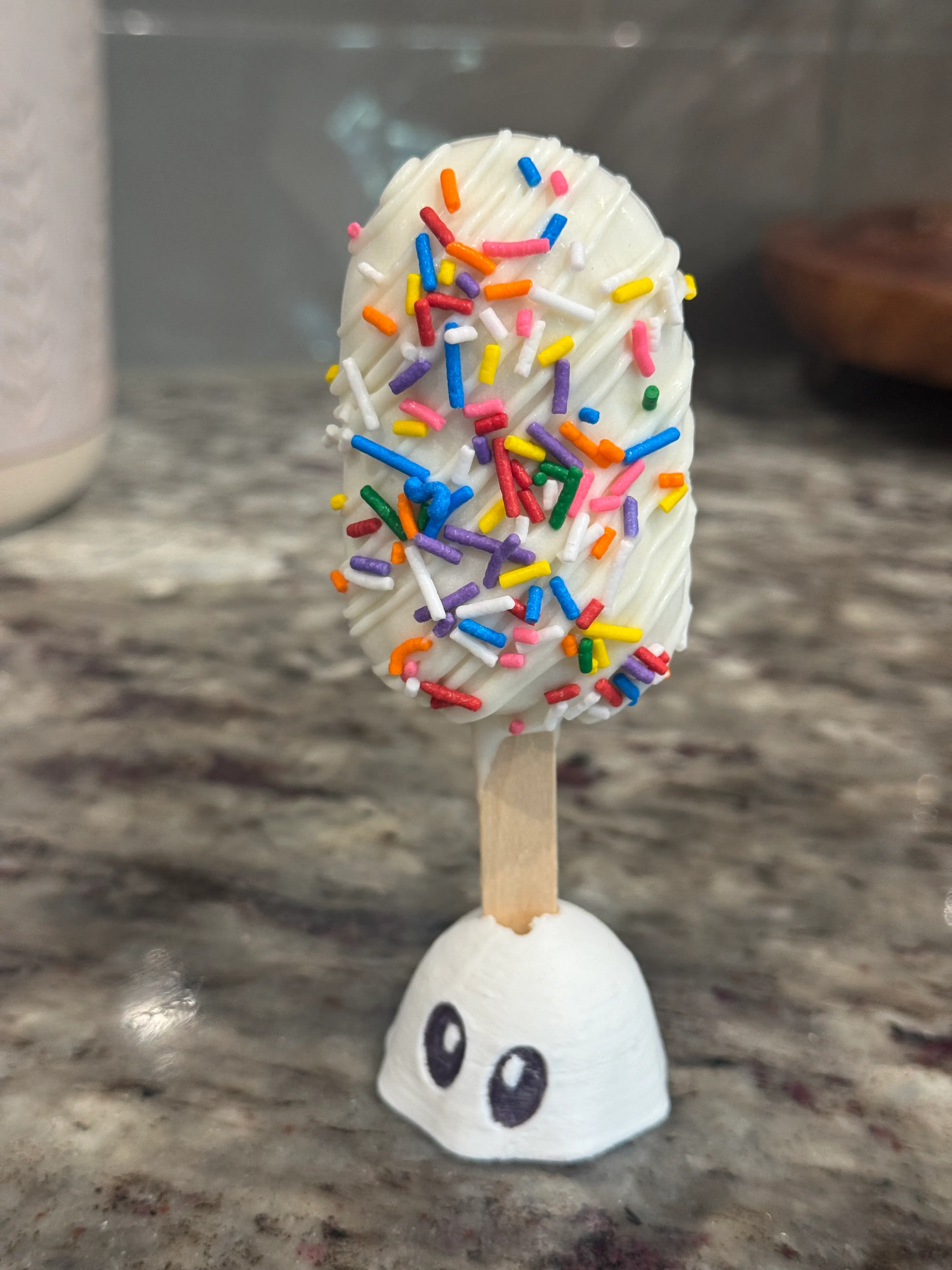 Dunkaroo cakesicle in a white shell with white drizzle and rainbow sprinkles