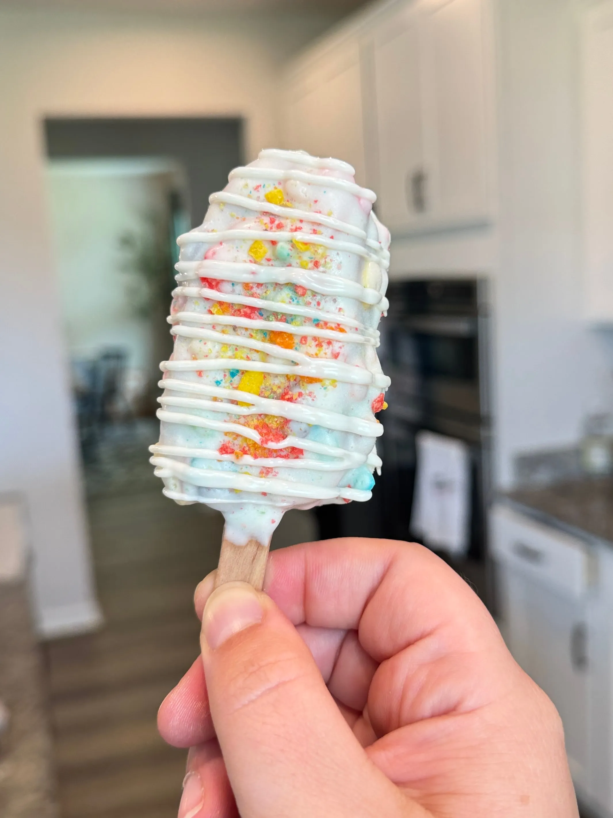 Fruity Pebbles cakesicle packed with cereal pieces under a white shell and drizzle