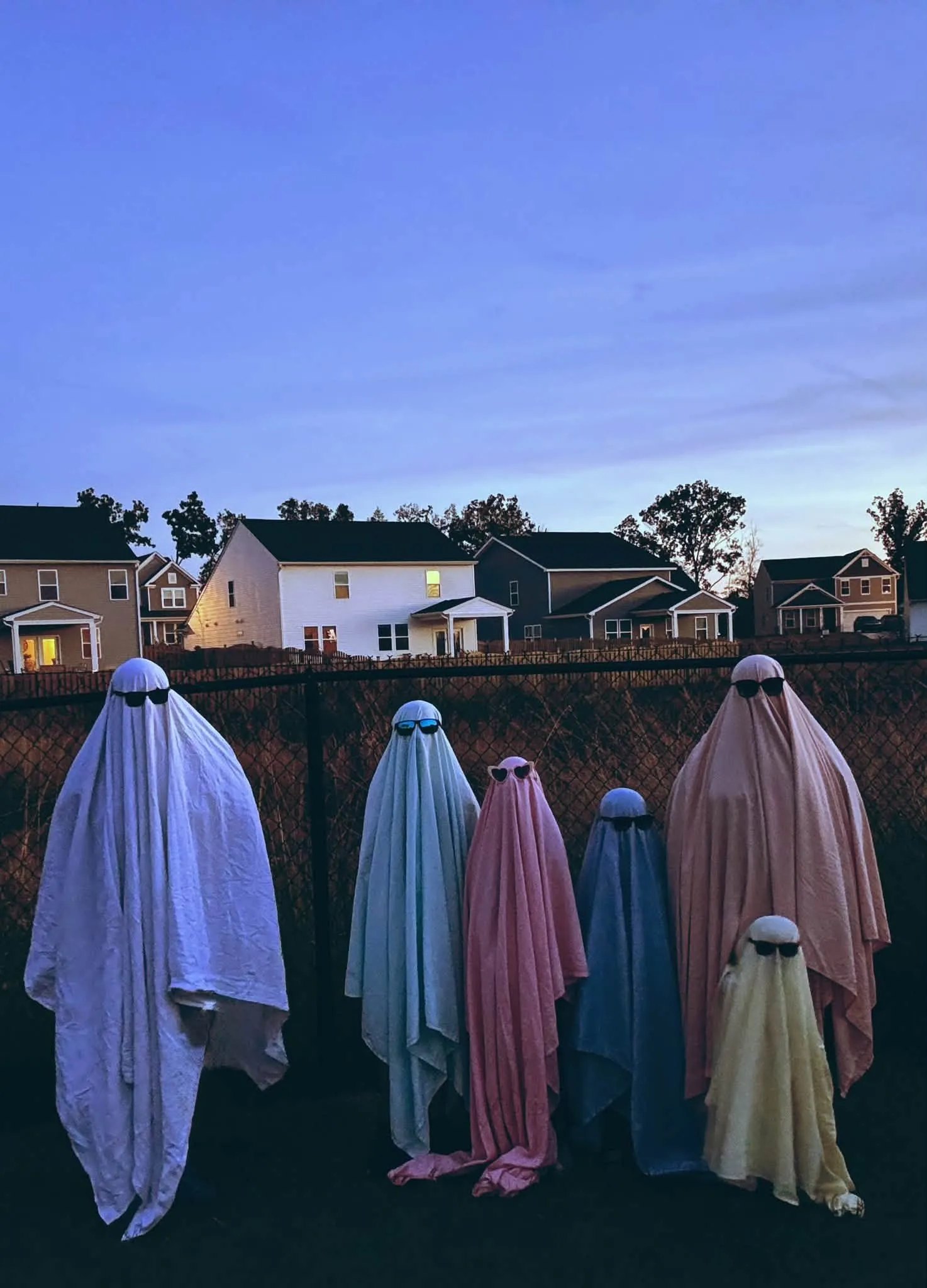 Six pastel sheet ghosts in sunglasses lined up at dusk
