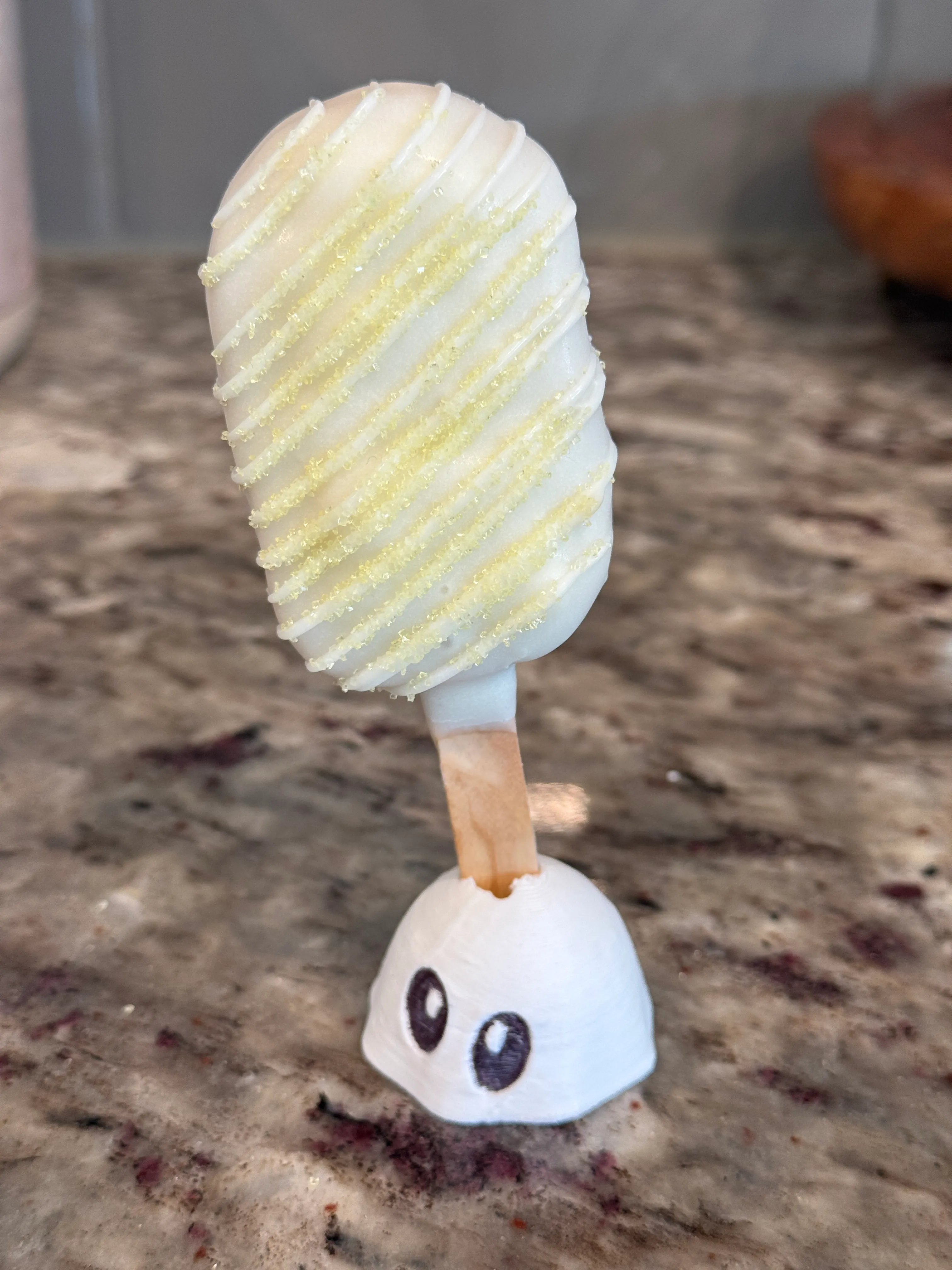 Lemon creme cakesicle in a white shell with white drizzle and yellow sanding sugar