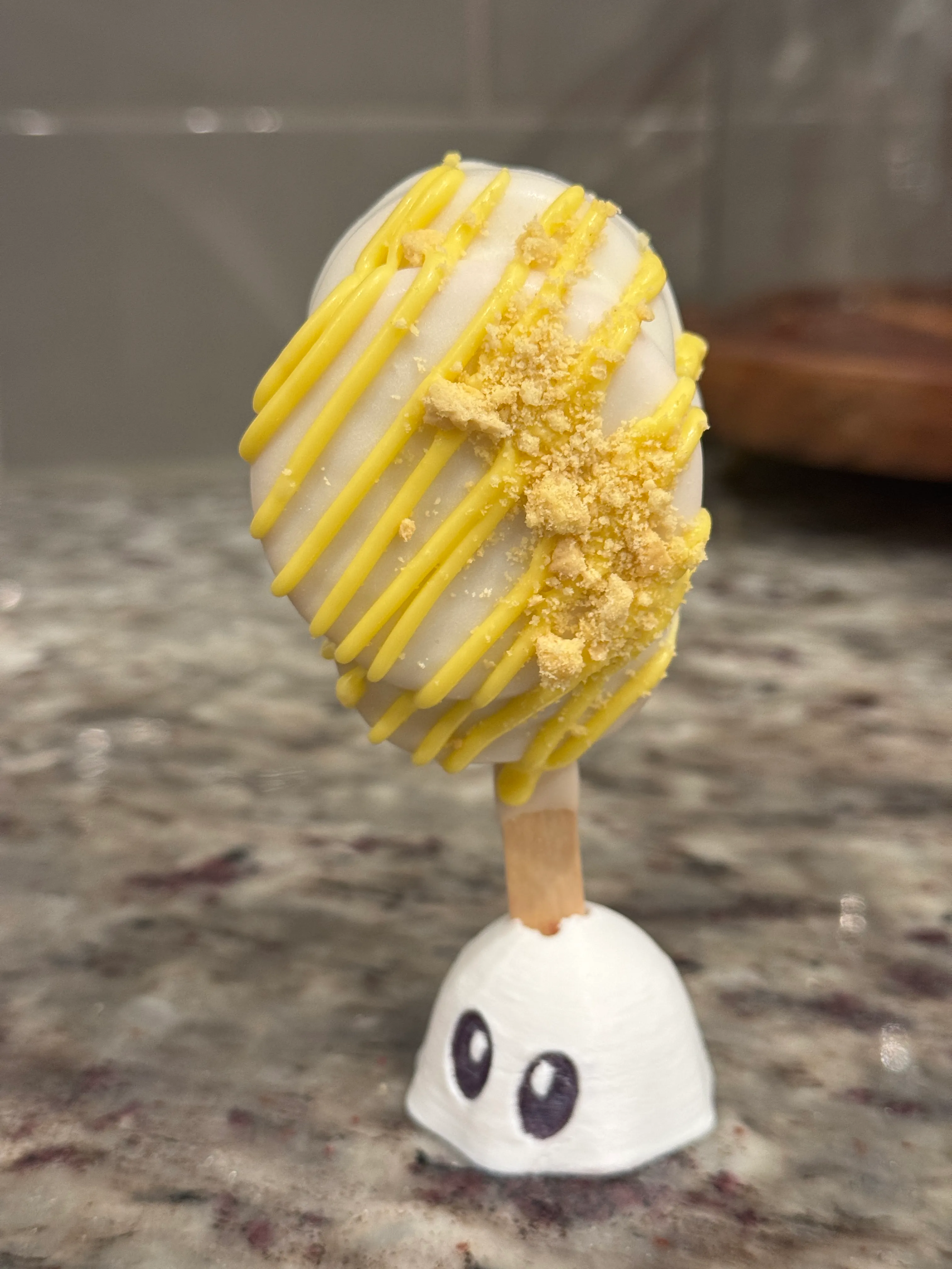 Lemon cookie crunch cakesicle in a white shell with yellow drizzle and lemon cookie crumbs