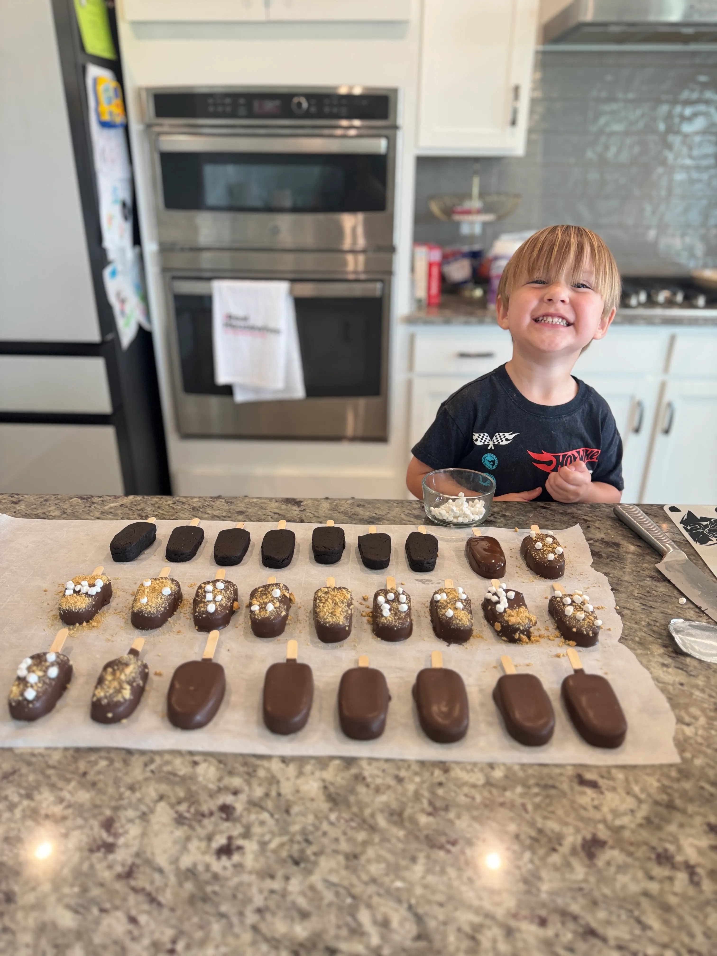 Liz’s helper grinning behind trays of freshly dipped cakesicles