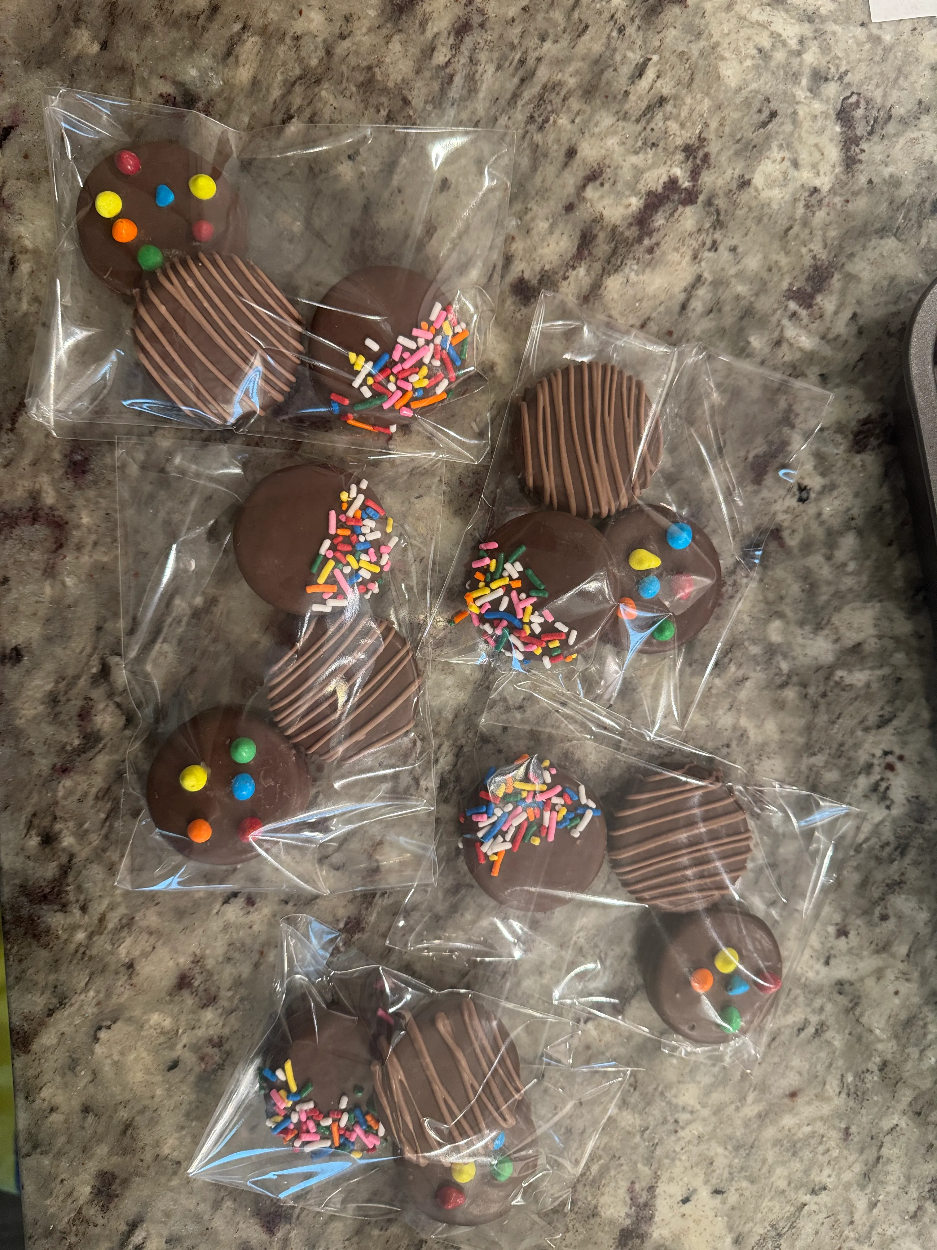 Chocolate dipped Oreos in sealed packs, decorated with rainbow sprinkles, candy pieces and chocolate drizzle