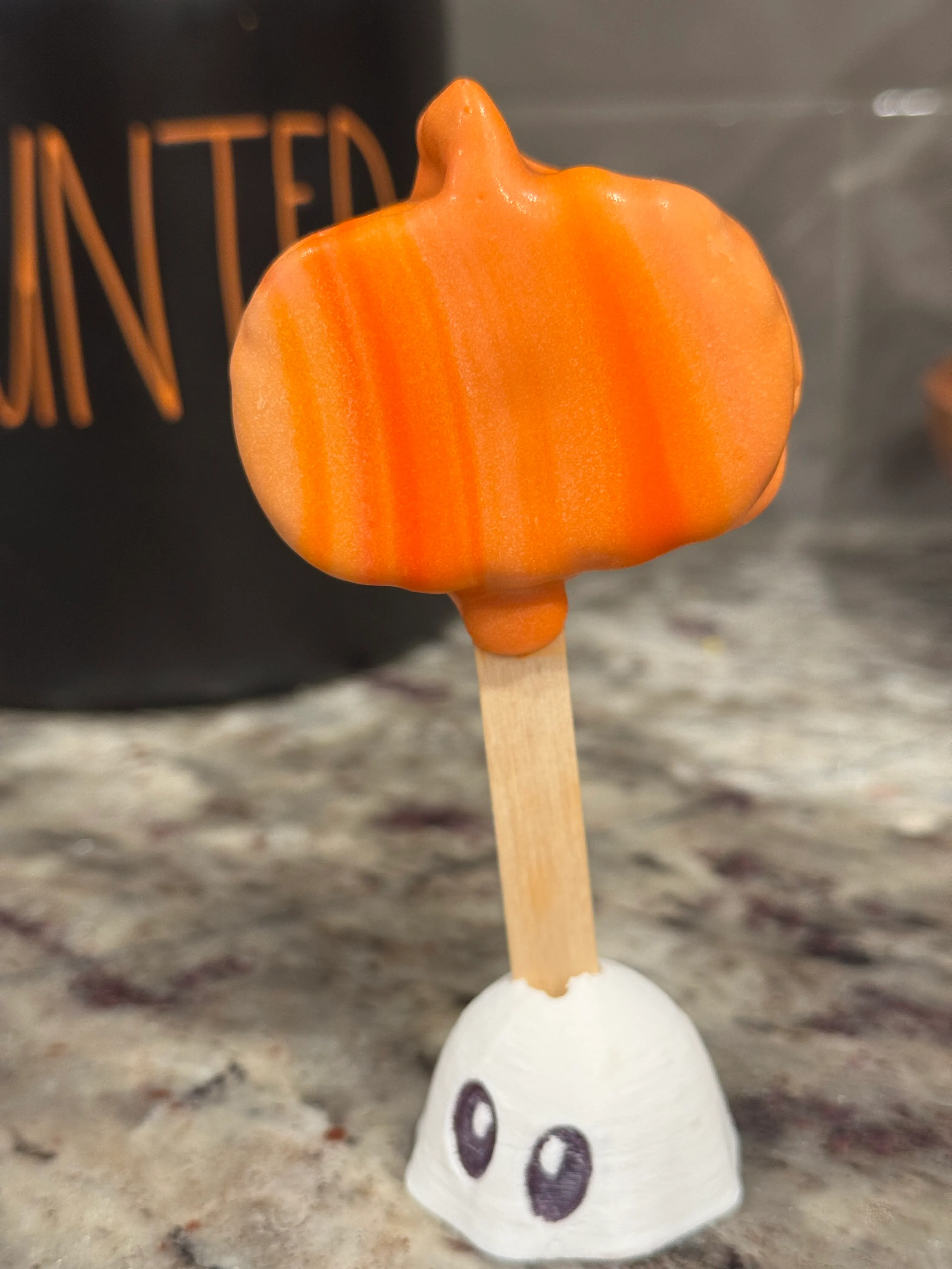 Pumpkin spice cakesicle shaped like a pumpkin with a stem, in an orange shell with darker orange ribbing