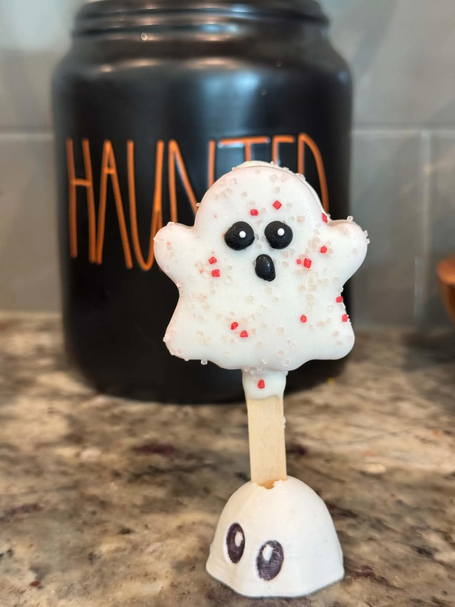 Strawberries and Scream ghost cakesicle in a white shell with pink and red sprinkles, with candy eyes and an open mouth